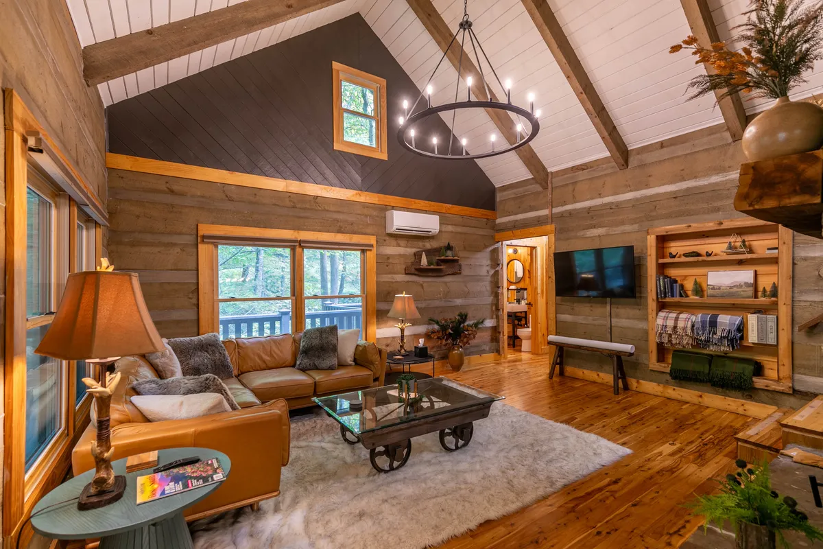 A warm, inviting living area featuring a leather sofa, a chandelier, a coffee table, and bookshelves. The mood is relaxed and social, ideal for gathering with family or friends for board games or casual entertainment.
