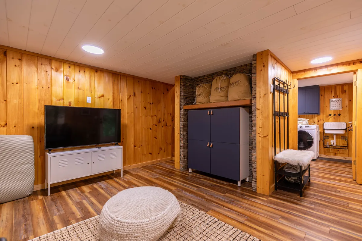 A multifunctional interior space that includes a television, a storage cabinet, a washing machine, and a seating area. The setup suggests a practical and welcoming environment where family members can gather to watch movies or play games.